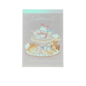 Front view of a mini memo pad on a black background with an iridescent top border. Features Sugar Cocomuu standing on a sweet-filled dessert stand with pastel animal companions.