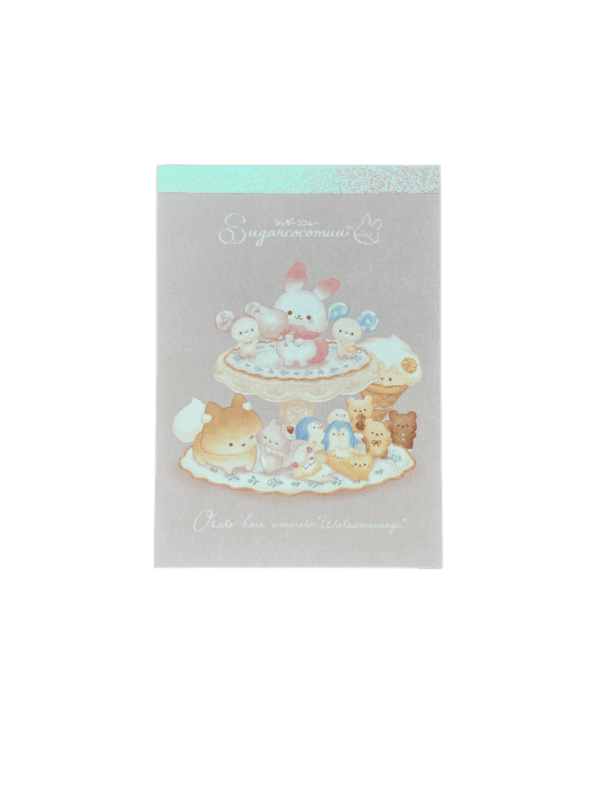 Front view of a mini memo pad on a black background with an iridescent top border. Features Sugar Cocomuu standing on a sweet-filled dessert stand with pastel animal companions.